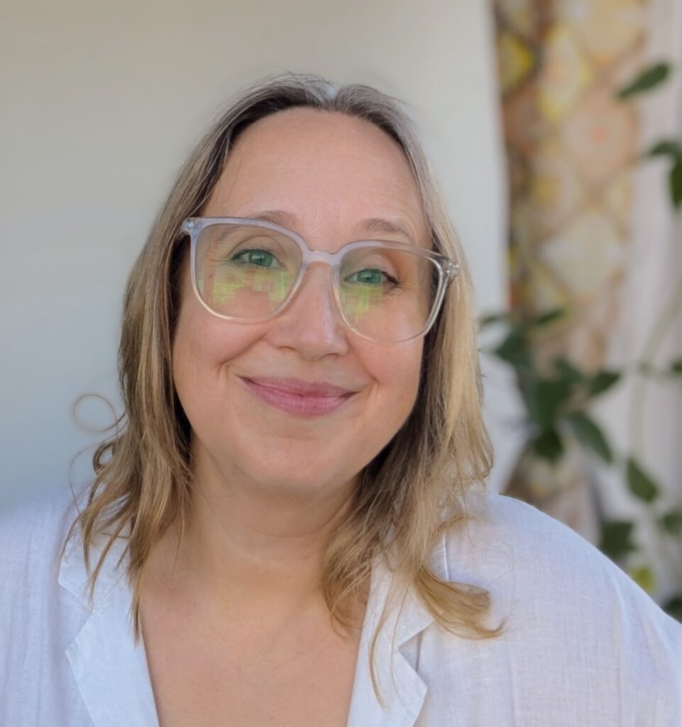 Rachel Thompson Writing Courses | Rachel wears a white shirt, large glasses, and has grey-yellow, shoulder-length hair.