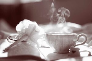 Teacup steaming in morning light on a notebook with written pages and with a pink flower-pen on top.