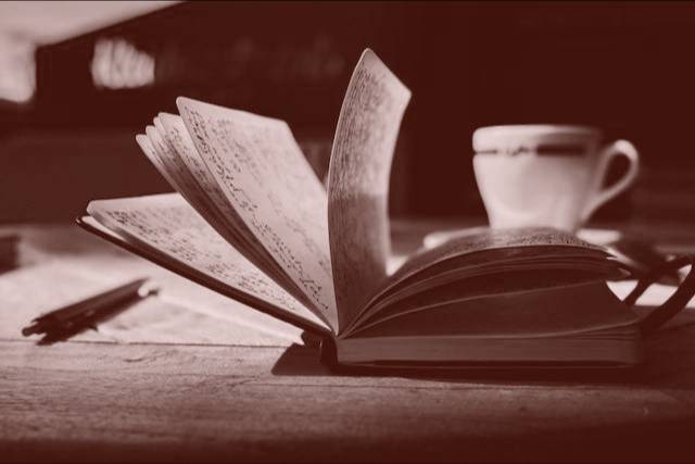 An open notebook with pages flipping. A pen on a table. A coffee cup in the background.