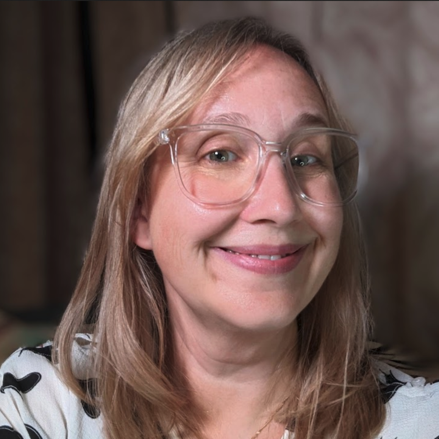 Rachel Thompson has light straight shoulder-length hair and wears a black and white shirt with stylized hearts on them, and clear big-framed glasses as she slightly smiles in this photo.
